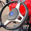 Close-up of a red tractor cockpit: black steering wheel with a silver center and blue emblem, with dashboard gauges in the background.