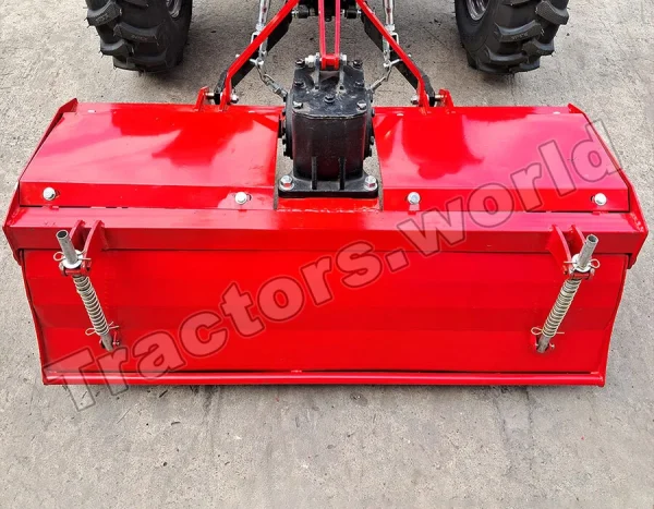 Red agricultural implement attached to a tractor, viewed from the front on a concrete surface with large tires visible above and a central hitch assembly.